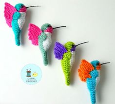 three crocheted hummingbirds hanging from strings on a white surface, one is multicolored