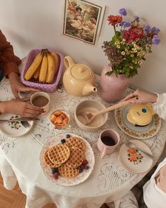 two people are sitting at a table with breakfast foods on it, including waffles and bananas