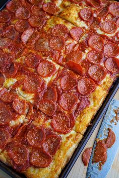 pepperoni pizza sitting on top of a pan next to a knife and spatula