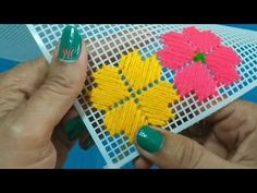 two hands are holding small pieces of colorful string art with green nail polish on them