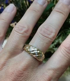 a woman's hand with a gold ring on it and flowers in the background