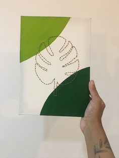 a hand holding up a piece of paper with a drawing on it that is green and white