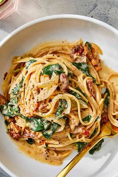 a white bowl filled with pasta and spinach on top of a marble countertop