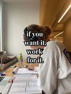 a woman sitting at a desk with papers and pens in front of her, looking out the window