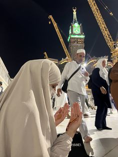 two women are praying in front of the clock tower and other people standing around them