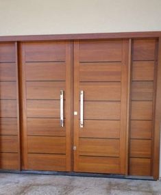 two large wooden doors in front of a white wall and concrete flooring with no one standing on it