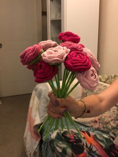 a woman is holding a bouquet of crocheted flowers in her hand while sitting on the bed