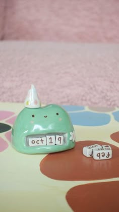 a green whale shaped toy sitting on top of a bed next to two dice numbers