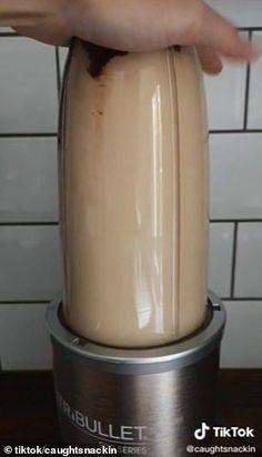 a person is pressing the button on a blender in front of a tiled wall