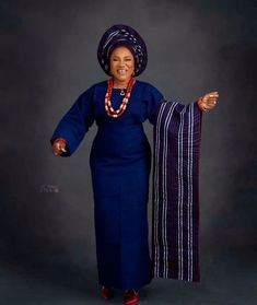 an african woman in a blue dress and beaded necklace holding up a purple scarf