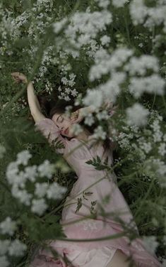 a woman is laying in the grass with her arms up and head down, surrounded by white flowers