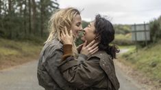 two women hugging each other on the side of a road in front of some trees