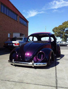 an old purple car parked in a parking lot next to a black and white car