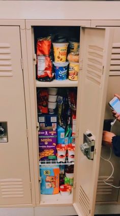 a man holding a smart phone next to a metal locker filled with food and drinks