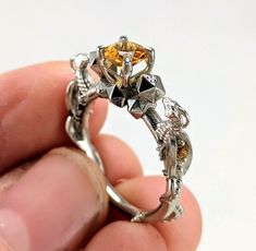 a person holding a ring with an orange diamond in it