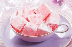 a bowl full of sugar cubes sitting on top of a purple saucer next to pink flowers