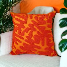 an orange pillow sitting on top of a white couch next to a potted plant