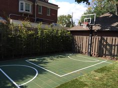 an outdoor basketball court in front of a house with a fence and trees around it