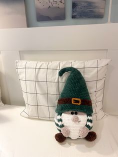 a crocheted gnome pillow sitting on top of a bed next to two pictures