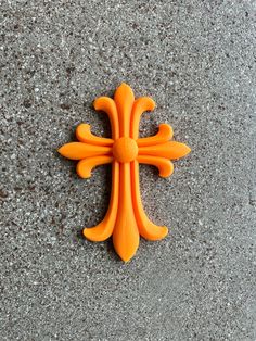 an orange plastic cross sitting on top of a cement floor next to a black and white wall