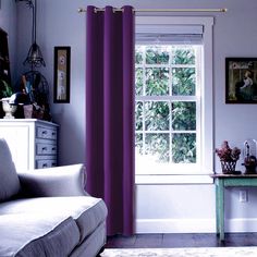 a living room filled with furniture and a window covered in purple drapes next to a white couch