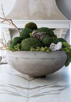 a large bowl filled with green plants on top of a white marble counter next to a fireplace