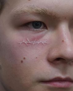 a young man with barbed wire on his forehead looks at the camera while he is wearing an eyeliner