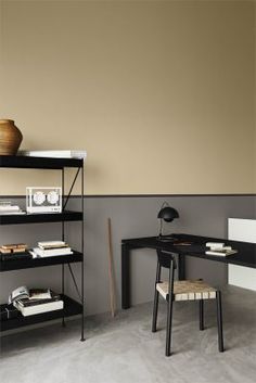 a black desk and chair in a room with a brown wall behind it, next to a book shelf filled with books