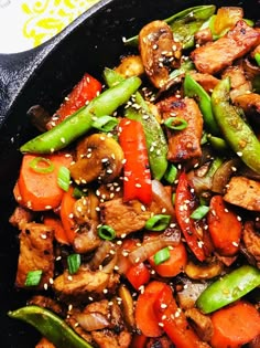 a skillet filled with meat and vegetables covered in sesame seeds