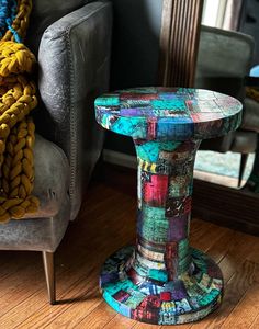 a colorful stool sitting on top of a hard wood floor next to a chair and mirror