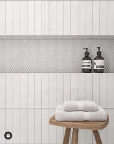 two white towels are sitting on a stool in front of a wall with hexagonal tiles