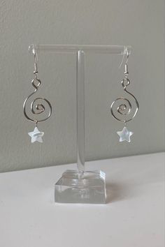 silver earrings with white stars hanging from them on a clear display stand in front of a gray wall