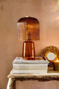 a lamp sitting on top of a table next to a stack of books and a mirror