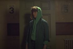 a person in a green coat standing next to a door with numbers on the wall