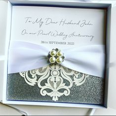 a wedding card in a box with ribbon and brooches on the front, attached to a bow