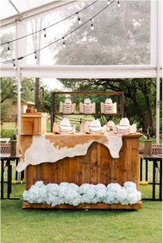 a wooden table topped with blue flowers under a white and brown tented area filled with food