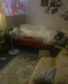 a room with a bed, fan and various pictures on the wall above it in front of a window