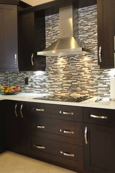 a kitchen with brown cabinets and stainless steel hood over the stove top, along with a bowl of fruit on the counter