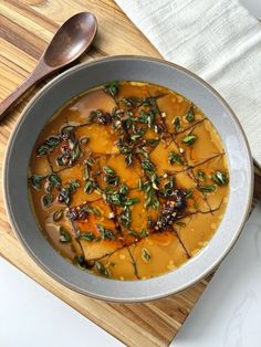 a bowl filled with soup on top of a wooden cutting board next to a spoon