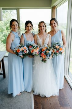 four bridesmaids pose for a photo in front of a large window