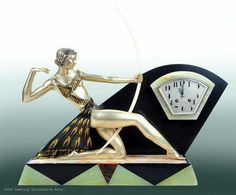 a gold and black clock with a woman dancing on it's face next to a wall clock