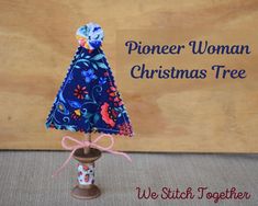 a small blue christmas tree on top of a wooden stand next to a sign that says pioneers woman christmas tree