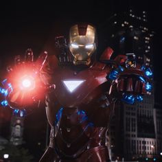 iron man in the middle of a city at night with lights on his chest and arm