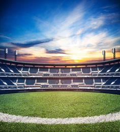 an empty baseball stadium with the sun setting in the background and grass on the field