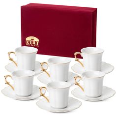 six white cups and saucers with gold trimmings in front of a red box