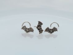 two silver earrings with bats on them sitting on top of a white surface and facing the camera