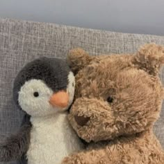 two stuffed animals sitting next to each other on a couch with one penguin hugging the other