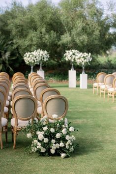 rows of chairs with white flowers and greenery on the grass in front of them