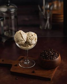 two scoops of ice cream sit in a glass bowl next to coffee beans on a cutting board