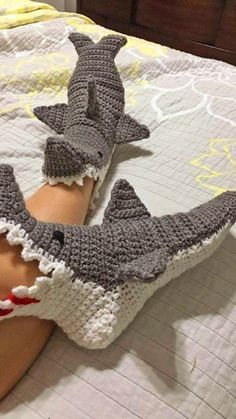 two crocheted shark gloves laying on top of a person's leg in bed